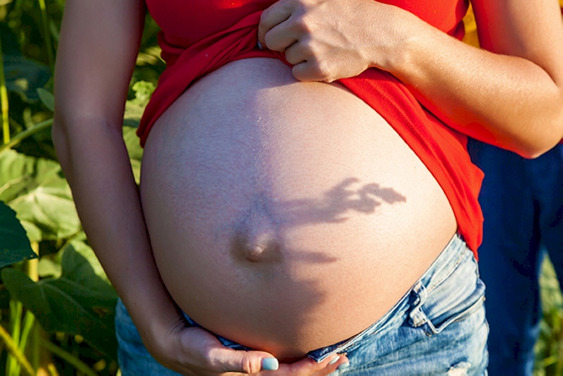 Pregnant girl in nature. Photoshoot of a pregnant girl in jint and red t-shirt in a field at sunset